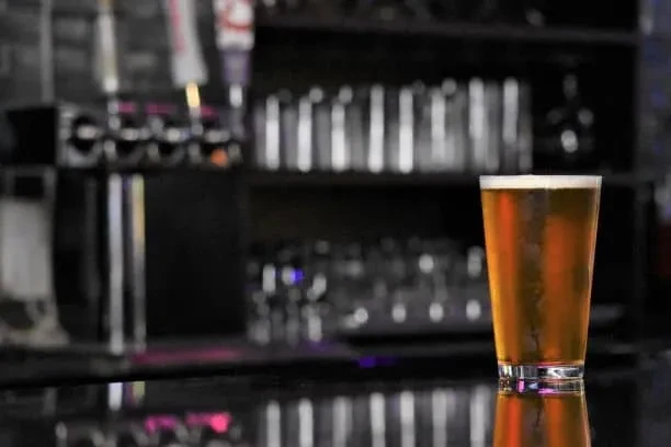 Pint of amber beer on a reflective bar with blurred taps.