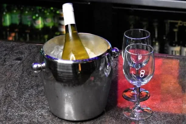 Chilled wine bottle in ice bucket, two glasses on granite counter.