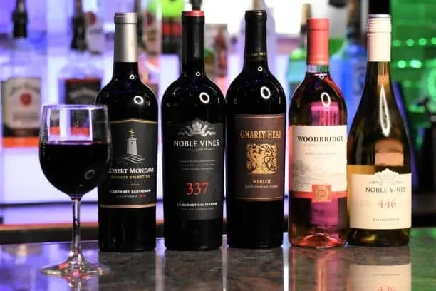 Five wine bottles and a glass of red wine on a reflective bar.