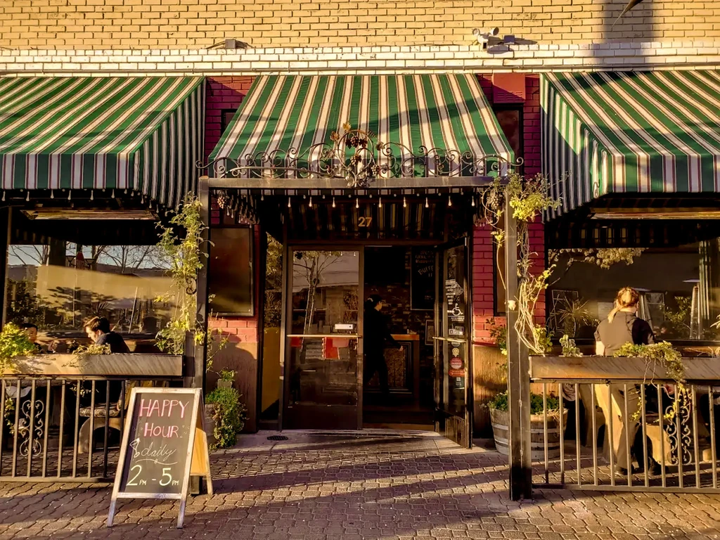Warmly lit brick restaurant '27' with green awnings and outdoor patio.