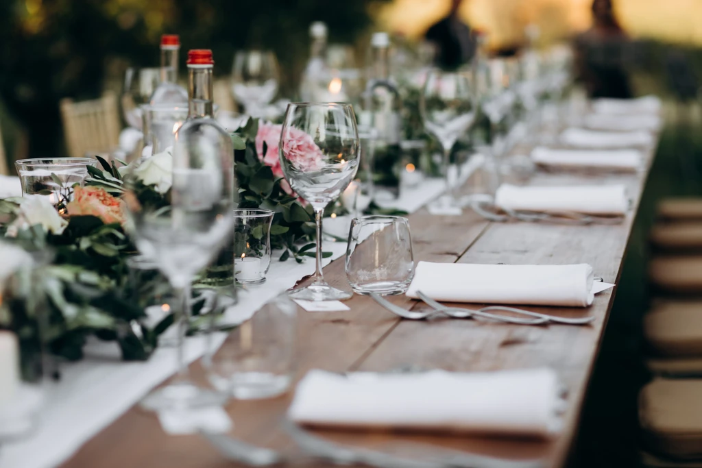 Long outdoor dining table elegantly set with flowers, candles, and glassware.
