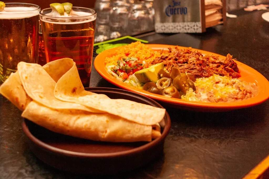 Shredded beef platter, tortillas, and two beers with lime wedges.