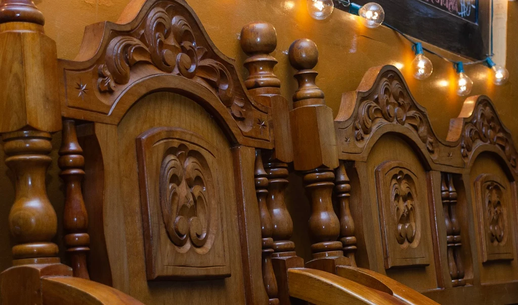 Elaborately carved wooden furniture with floral scrollwork, illuminated by globe lights.