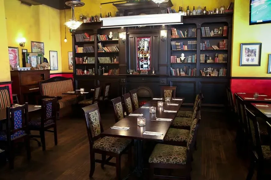 Library-themed restaurant interior with book-filled shelves, dining tables, and a piano.