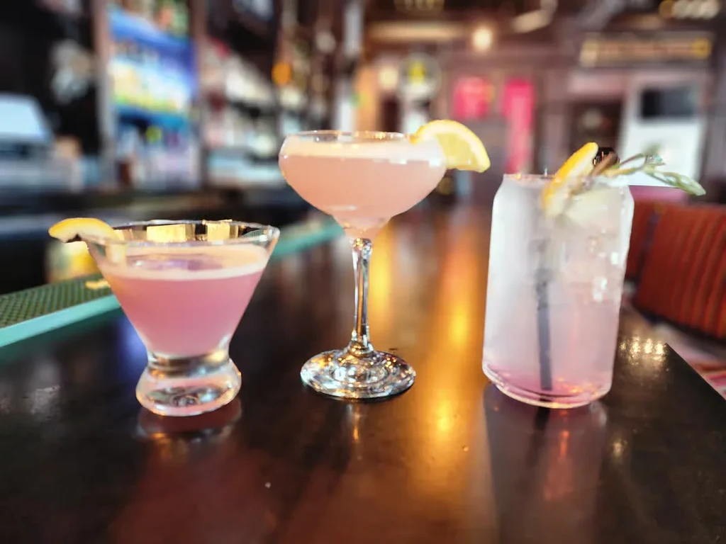 Three pink cocktails with lemon in different glasses on a bar.