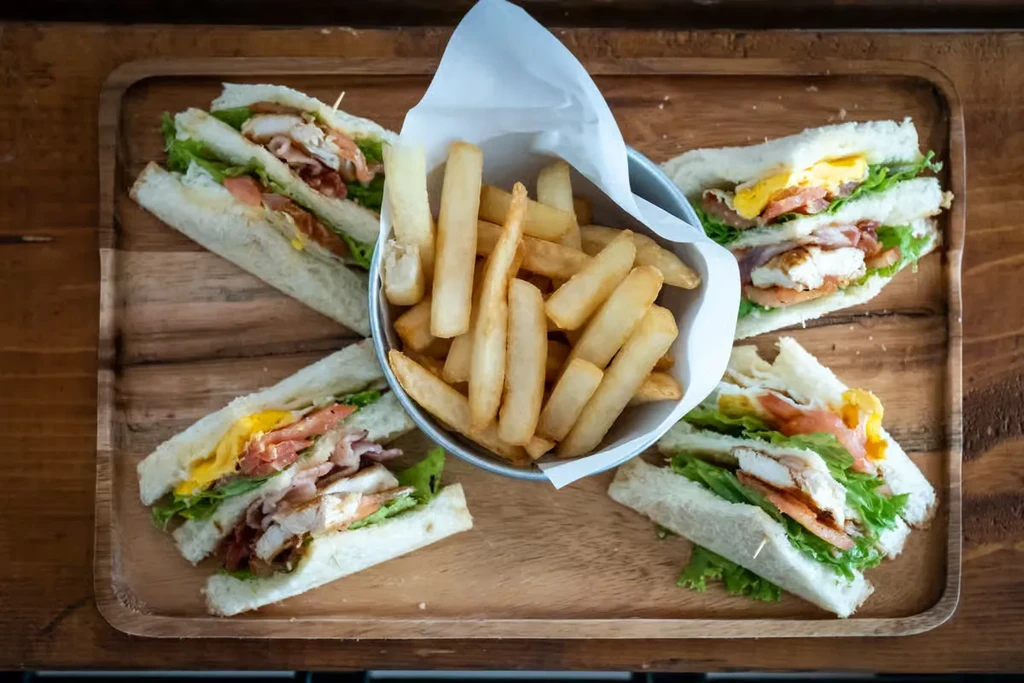 Close-up of club sandwiches and French fries on a wooden tray.