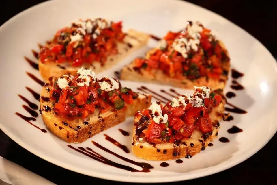 Four bruschetta topped with tomato, herbs, creamy cheese, and balsamic.