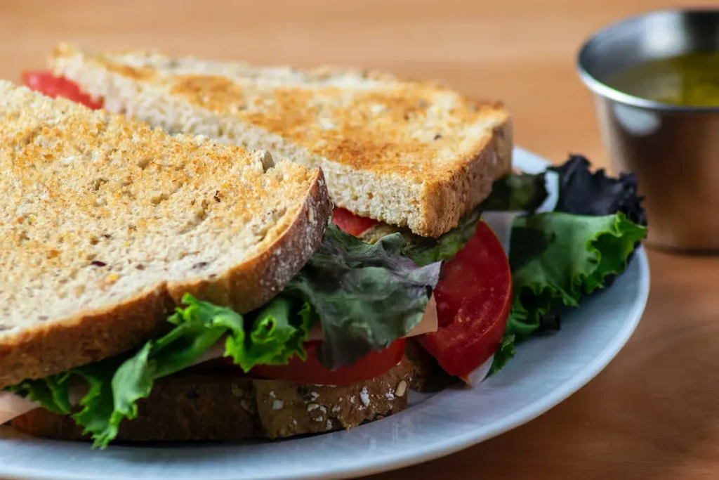 Toasted whole-grain sandwich cut in half, showing lettuce, tomato, and meat.
