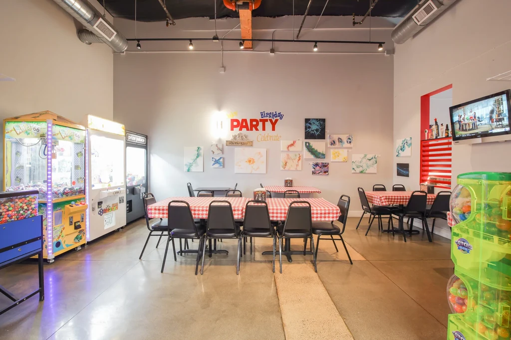 Modern party venue with arcade games and checkered dining tables.