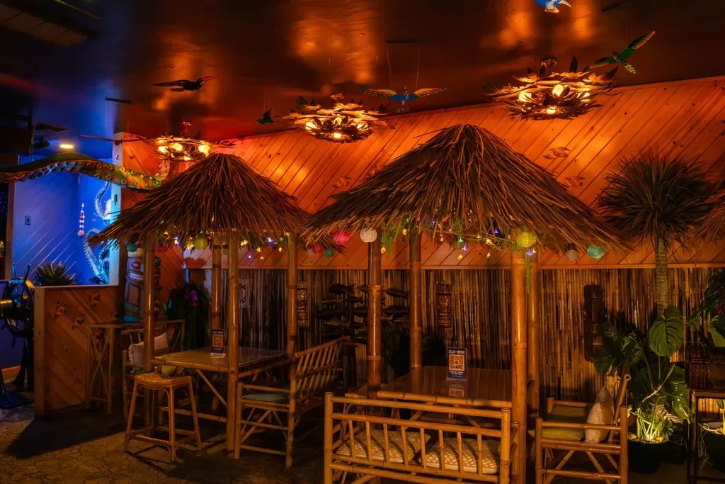 Tiki bar interior with bamboo seating, thatched roofs, and octopus mural.
