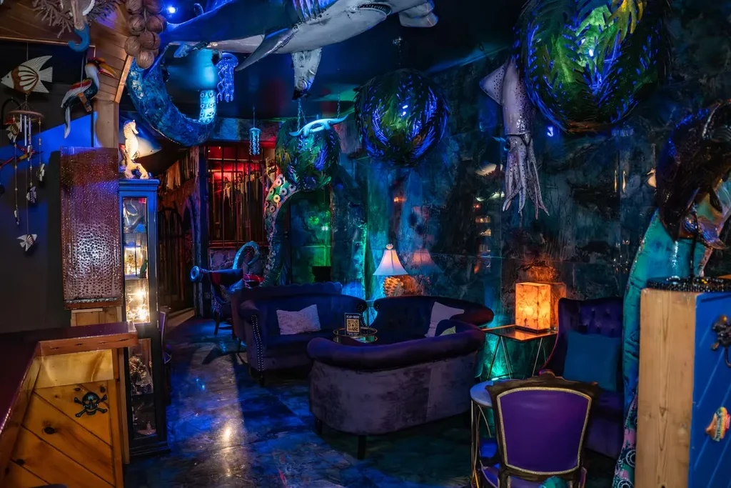 Deep-sea themed bar with blue lighting, marine sculptures, and velvet seating.