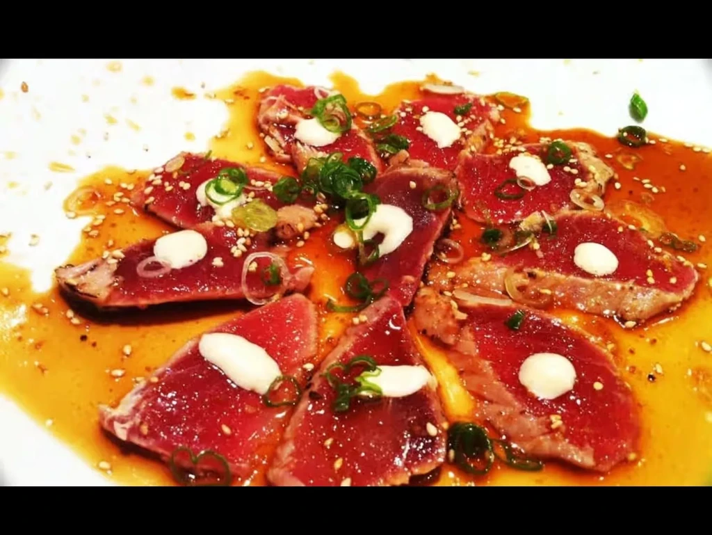 Seared tuna slices with sauces, green onions, and sesame seeds.