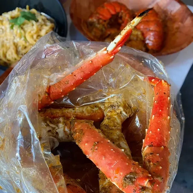 Seasoned red crab legs in a plastic bag with blurred pasta and seafood.