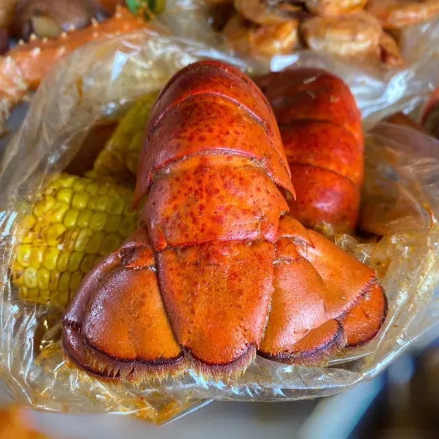 Cooked red-orange lobster tail and yellow corn in a clear plastic bag.