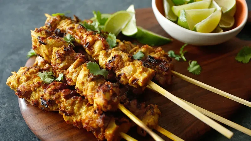 Golden-brown chicken skewers with cilantro and lime on a wooden board.