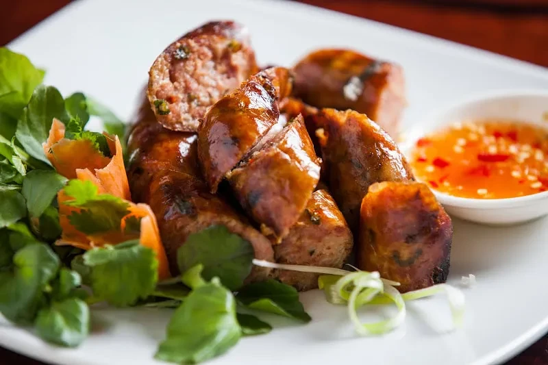 Plate of browned sausages with watercress, carrots, and chili dipping sauce.