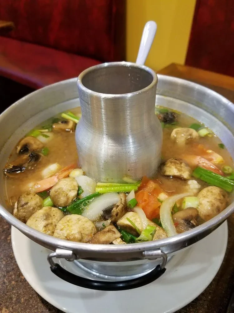 Traditional metal hot pot with shrimp, mushrooms, and vegetables.