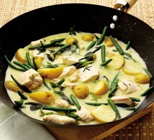 Creamy chicken and potato curry with green beans in a black wok.