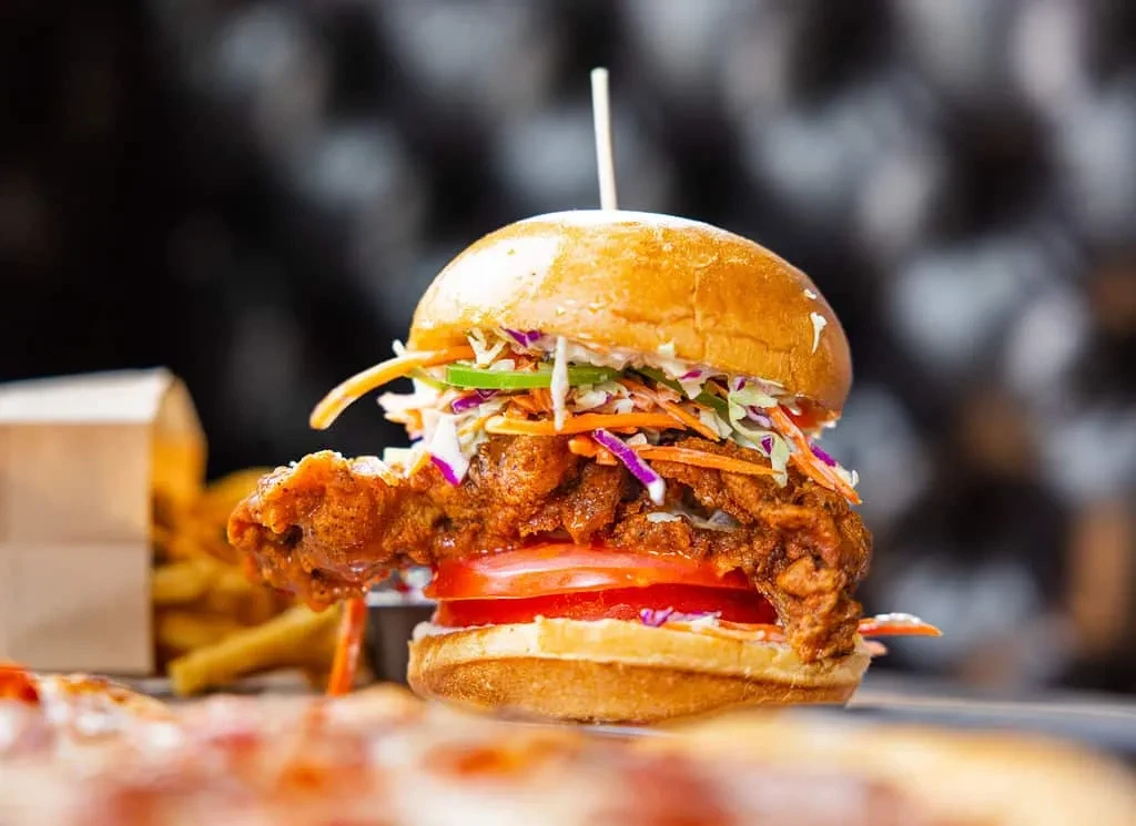 Crispy fried chicken sandwich with coleslaw, tomato, and blurred fries.