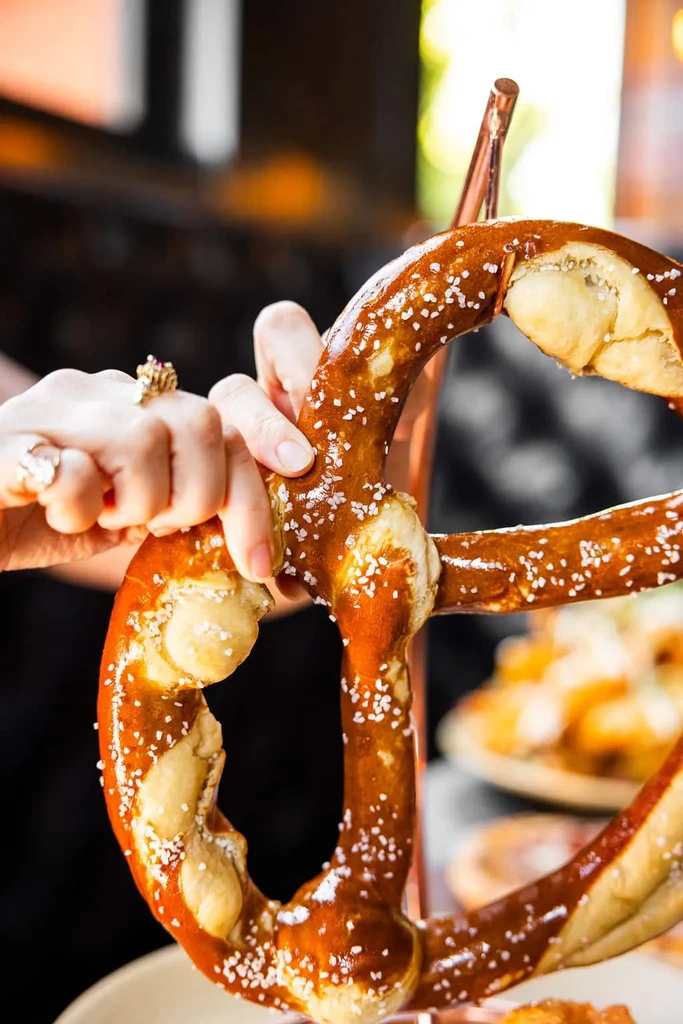 Golden-brown soft pretzel, generously salted, held by a ringed hand.