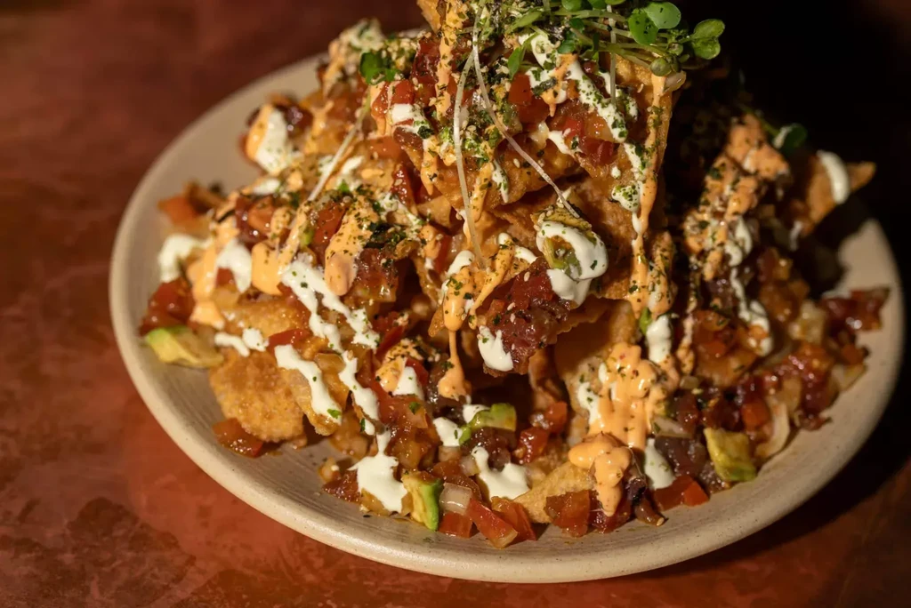 Loaded nachos with tomatoes, avocado, dark topping, sauces, microgreens.