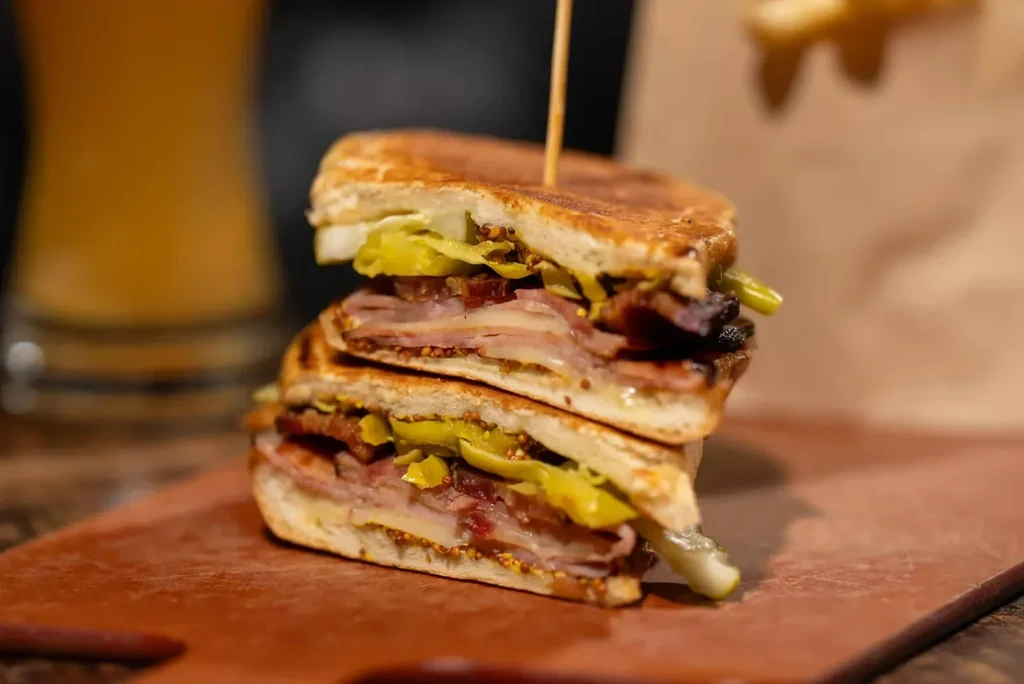 Cut pressed sandwich with ham, cheese, peppers on a cutting board.