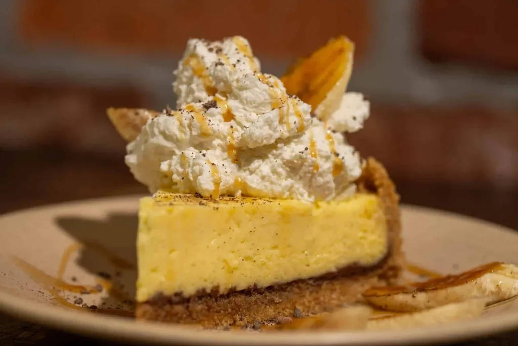 Creamy dessert slice with whipped cream, caramel, banana, and crumbs.