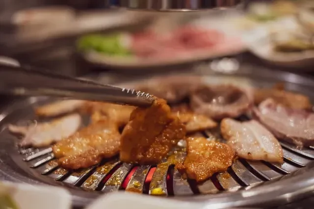 Cuts of meat sizzling on a Korean BBQ grill with tongs.