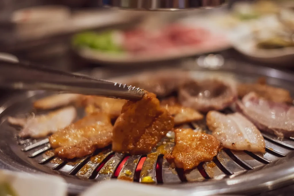 Marinated meat held by tongs grilling over red coals.