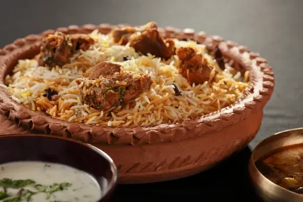 Biryani in a clay pot, served with raita and a brown curry.