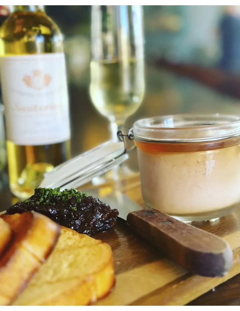 Close-up of toast, jam, pâté, and wine on a wooden board.