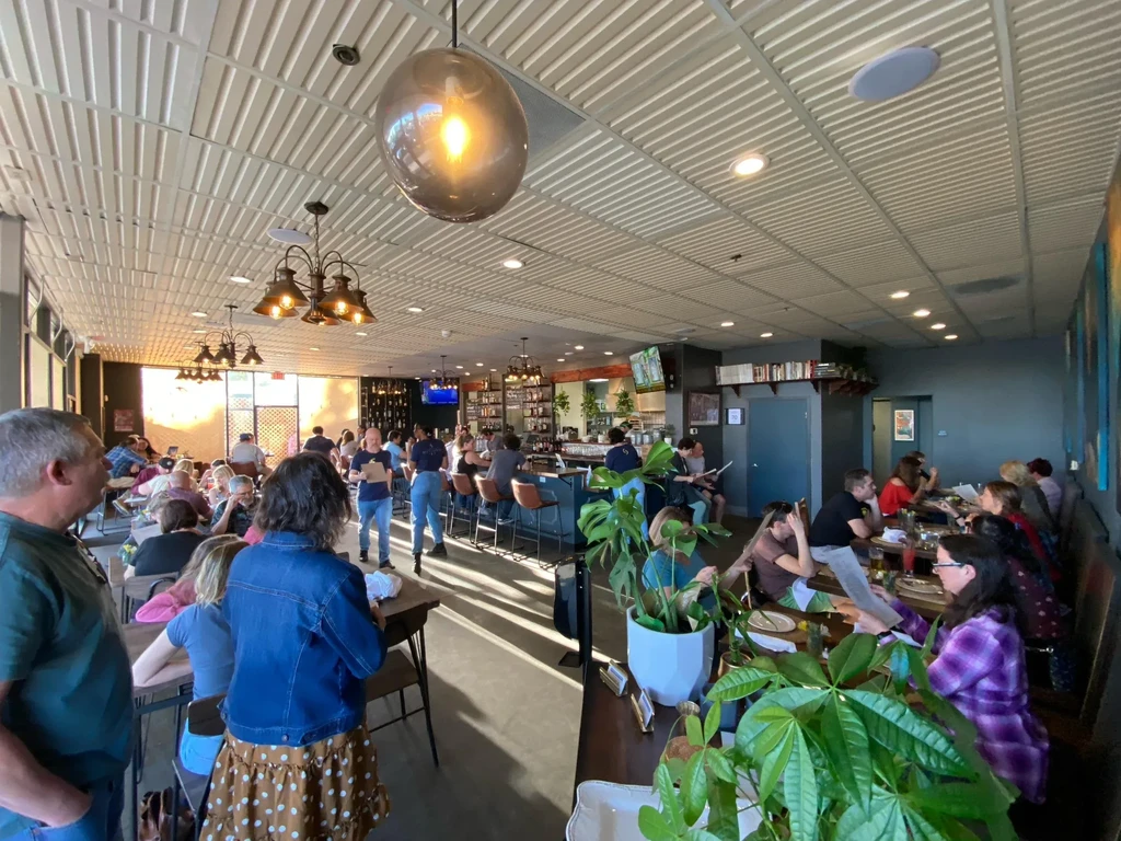 Bustling modern restaurant interior with patrons, bright light, and metal ceiling.