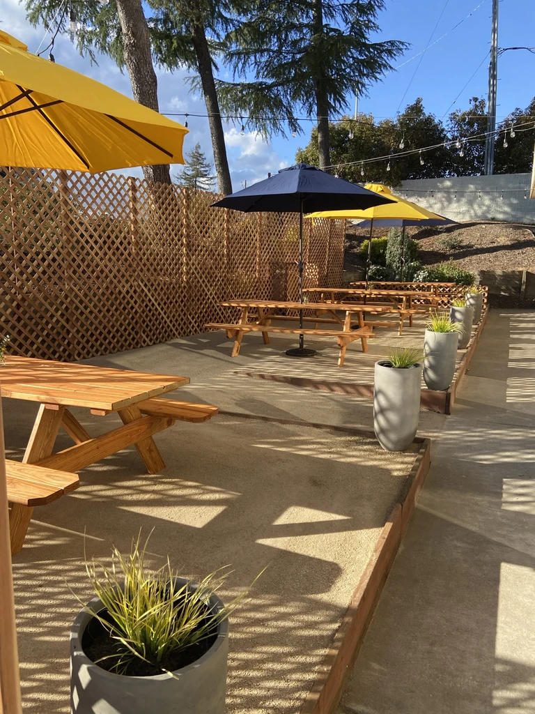 Outdoor patio with picnic tables, colorful umbrellas, and string lights.