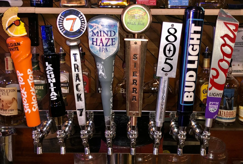 Seven distinctly branded beer tap handles in a bar.