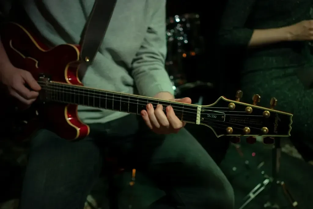 Close-up of musician playing a dark red electric guitar.