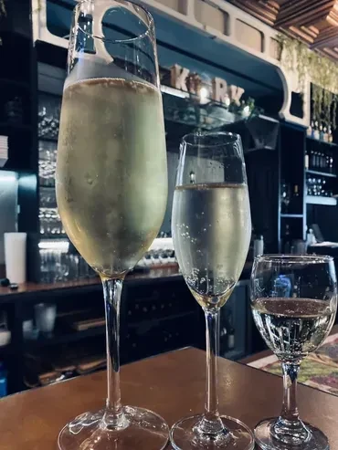 Three varying champagne flutes on a bar with a KORK sign.