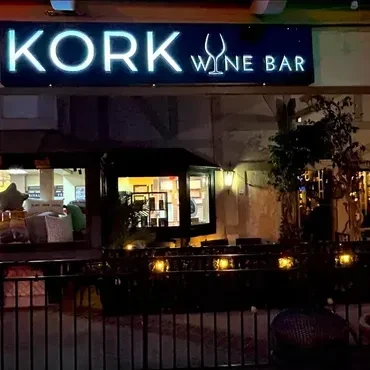 KORK WINE BAR neon sign glows above outdoor seating at night.