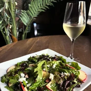 Salad with cheese, apple, and white wine on a wooden table.