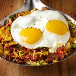 Breakfast hash with crispy potatoes, bacon, cheese, and bright sunny-side-up eggs.