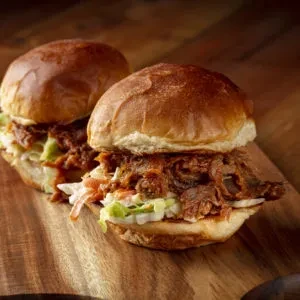 Two pulled pork and coleslaw sliders on a wooden cutting board.