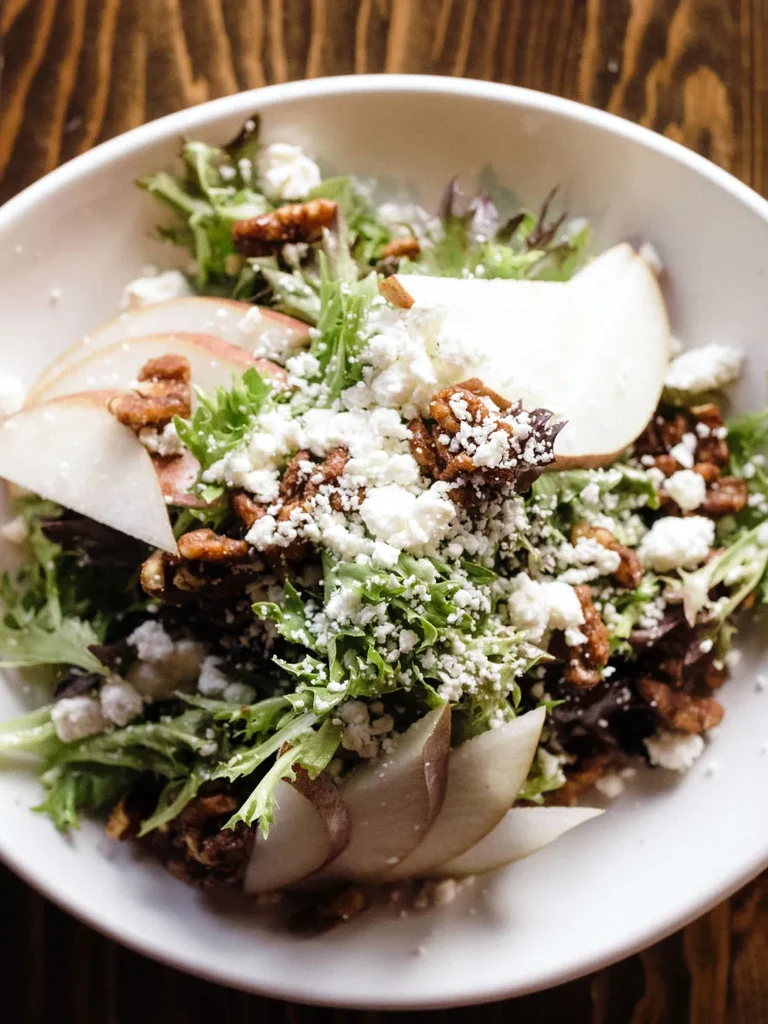 Close-up of fresh salad with greens, pears, cheese, and candied pecans.