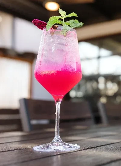 Vibrant pink gradient cocktail, garnished with dragon fruit and mint.