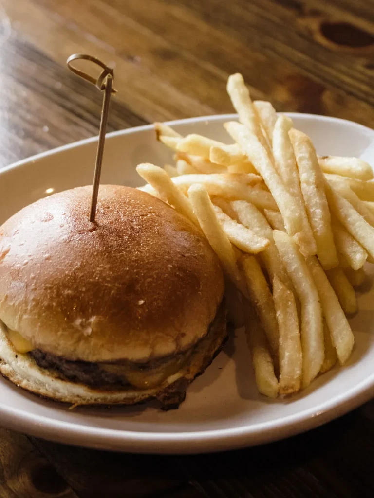 Close-up of a cheeseburger and golden fries on a white plate.