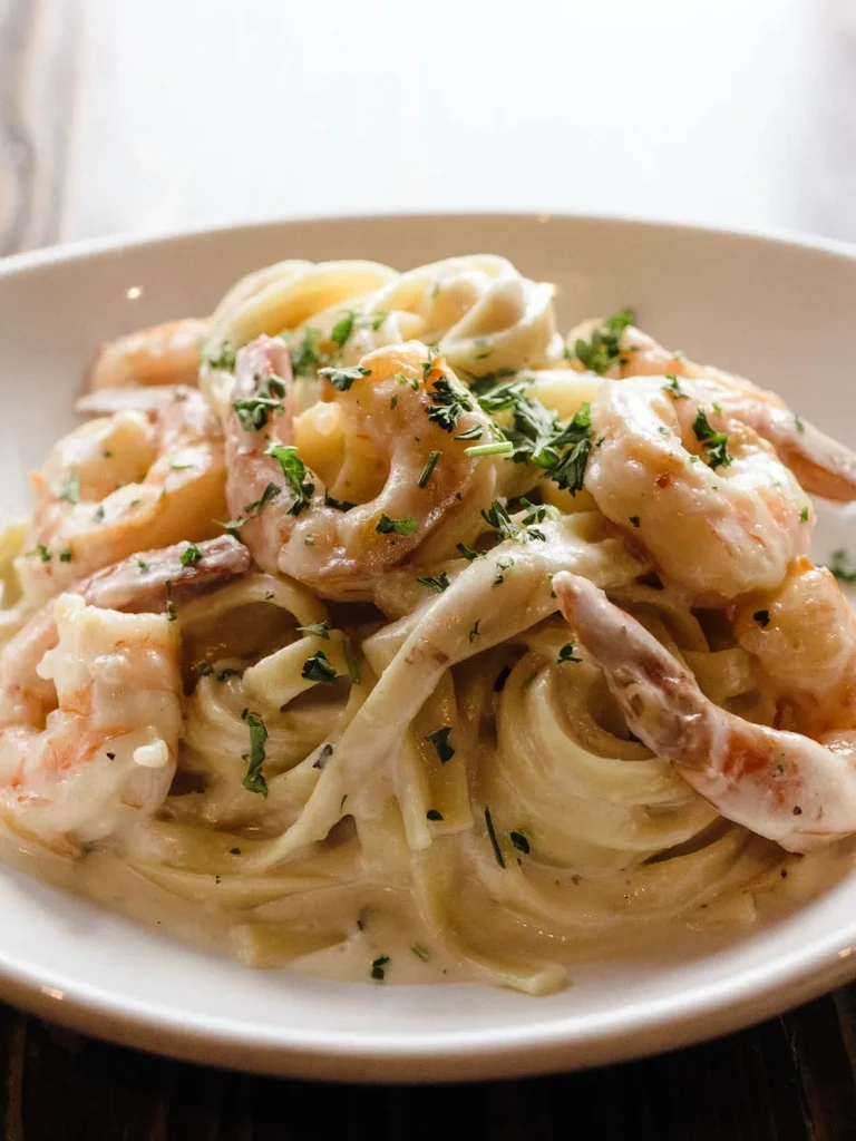 A bowl of creamy shrimp pasta garnished with fresh green herbs.