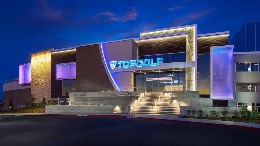 Modern Topgolf facility exterior at night with vibrant LED lighting.