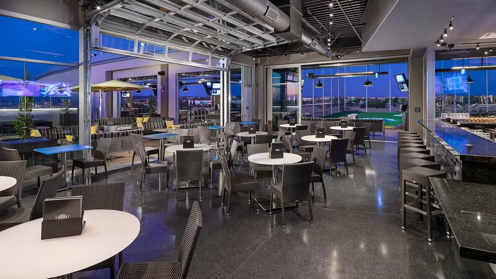 Modern restaurant bar, glass walls open to twilight golf range.