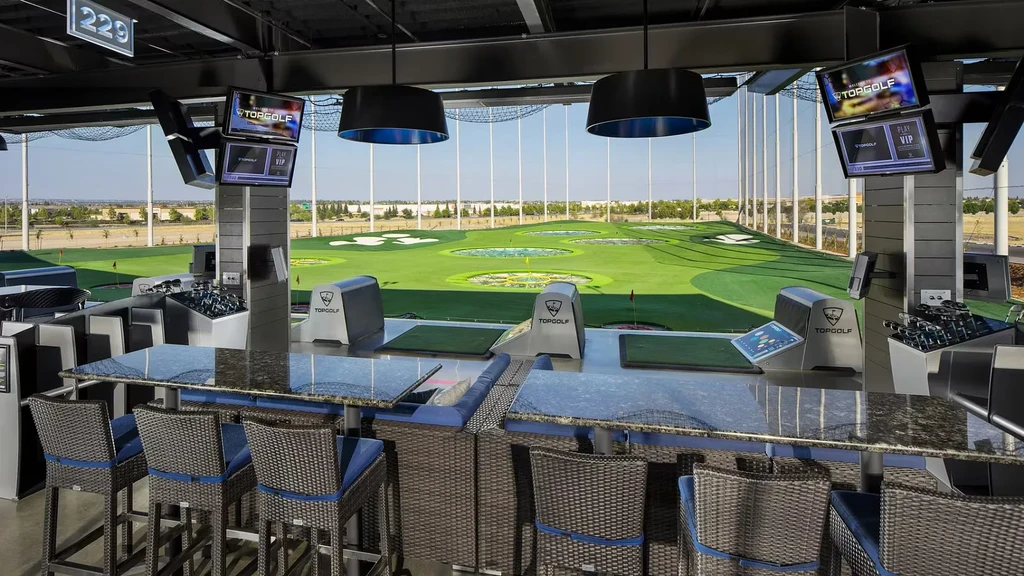 Empty Topgolf bay with seating, hitting mats, and driving range.