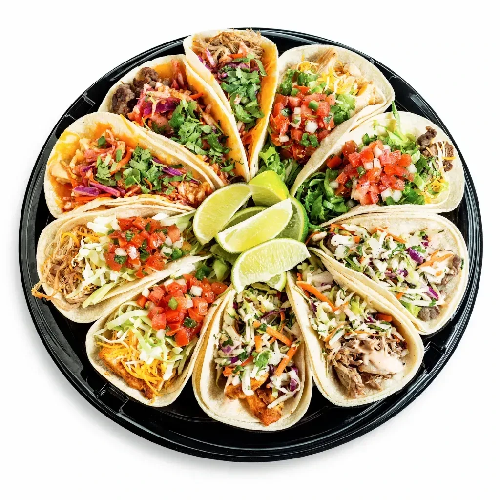 Twelve colorful tacos on a round black catering platter with lime.