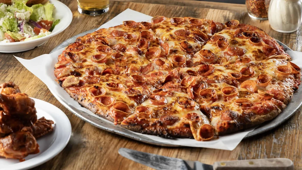 Pepperoni pizza, green salad, chicken wings, and beer on a wooden table.