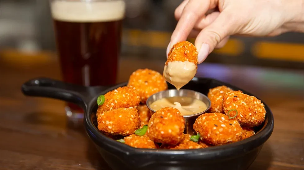 Hand dips golden breaded nuggets from a bowl into sauce.